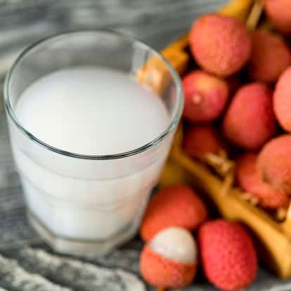 Lychee Juice in a short glass beside a basket of whole lychees on a wood surface