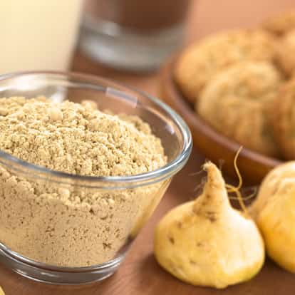 Maca Powder in a glass bowl with whole maca roots on a wooden surface