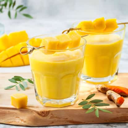 Mango Nectar in two glasses garnished with mango cube skewers on a wooden board