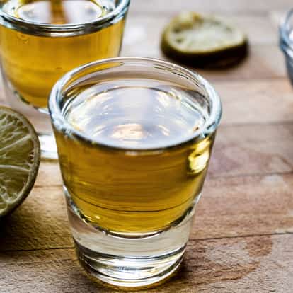 Mescal in a shot glass with lime halves on a wooden board
