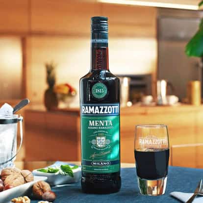 Mint Amaro bottle beside a glass of amaro with a mint sprig and a bowl of nuts on a table