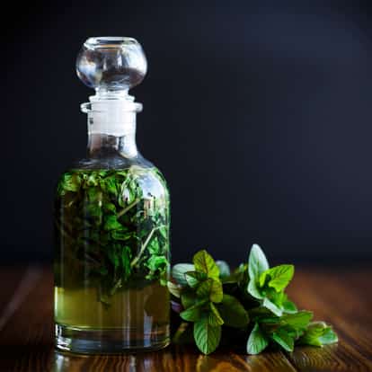 Mint Syrup stoppered glass decanter with steeped mint leaves and a sprig of mint on a wooden surface