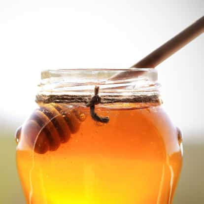 Orange Blossom Honey in a glass jar with a wooden honey dipper on white background