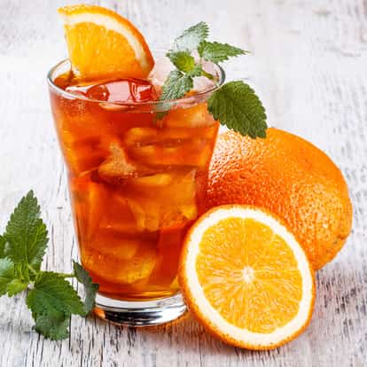 Orange Flavored Tea (hot) in a glass with ice, an orange slice and a mint sprig on a wooden surface