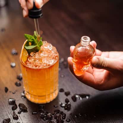Orange Flower Water in a rocks glass with crushed ice, mint and dried citrus wheel and a skull-shaped dropper bottle
