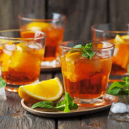 Orange Rum in a rocks glass with ice, an orange wedge and mint on a wooden board