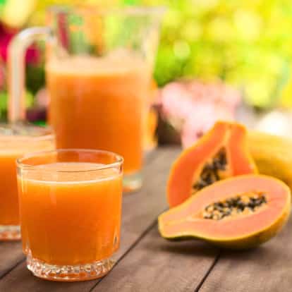 Papaya Juice in lowball glasses with a pitcher and halved papaya on a wooden table
