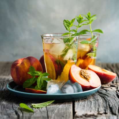 Peach Iced Tea in two glasses with ice, peach slices and mint sprigs on a ceramic plate