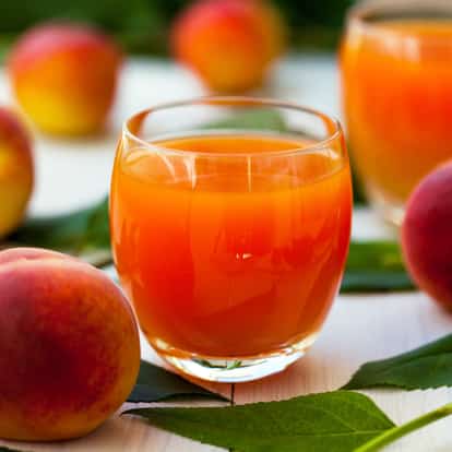 Peach Nectar in a stemless glass with whole peaches and leaves on white background