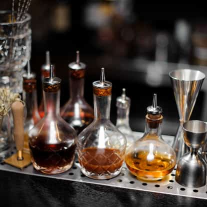 Peychaud's Bitters in glass bottles with metal pour spouts on a perforated steel bar tray