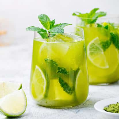 Pisang Ambon in two stemless glasses with lime wedges mint sprigs and ice on white background