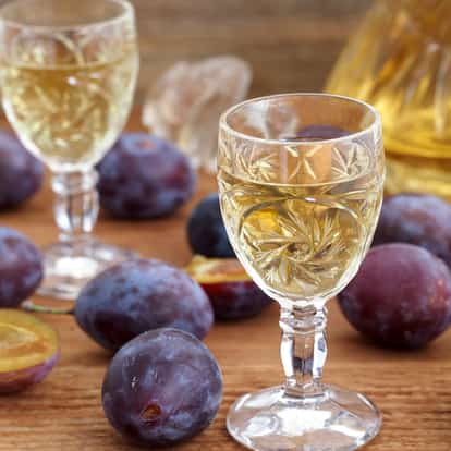 Plum Brandy in an engraved cordial glass with whole and halved plums on a wooden surface