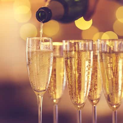 Prosecco pouring into a flute from a bottle with four filled flutes behind