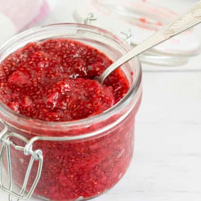 Raspberry Puree in a glass jar with a metal spoon on a white background