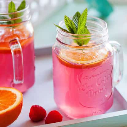 Raspberry Soda in a mason jar with an orange slice and mint sprig on a tray with two raspberries