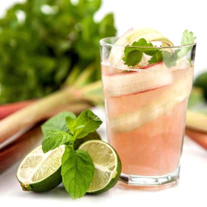 Rhubarb liqueur in a glass with rhubarb ribbon and mint sprig and lime halves on white background