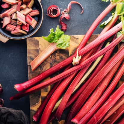 Rhubarb stalks and chopped pieces on a wooden cutting board with a small bowl