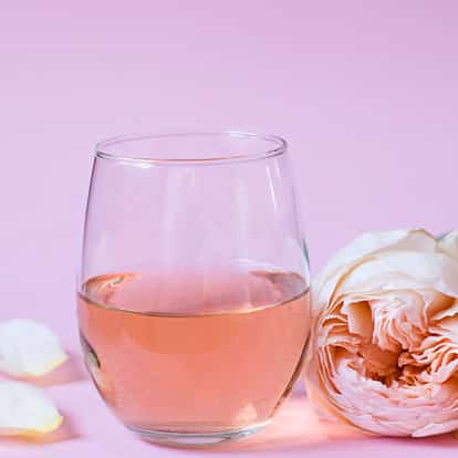 Rosewater in a stemless wine glass with a rose bloom and loose petals