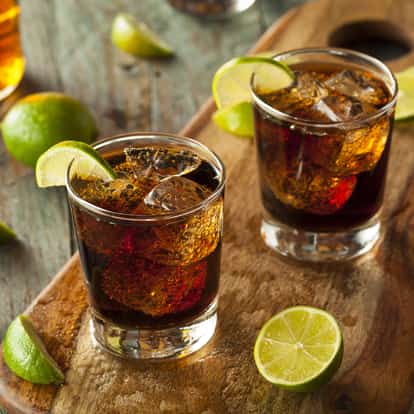Haitian Rum in two rocks glasses with ice and lime wedges on a wooden board