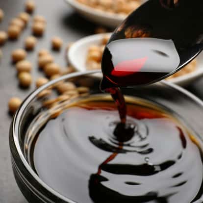 Soy Sauce poured from a spoon into a glass bowl with soybeans and small dishes in the background