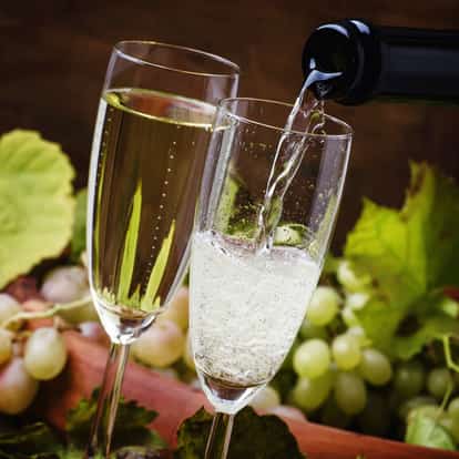 Sparkly grape two champagne flutes one being filled from a bottle with grape clusters in background
