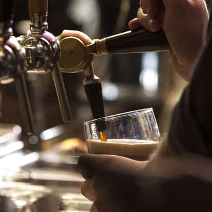 Stout Beer pouring from a tap into a tilted pint glass held by a hand
