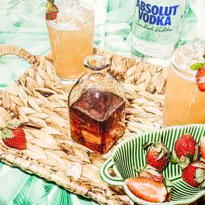 Cocktails in glasses with ice and strawberry beside an Absolut Vodka bottle and a bottle of strawberry liqueur