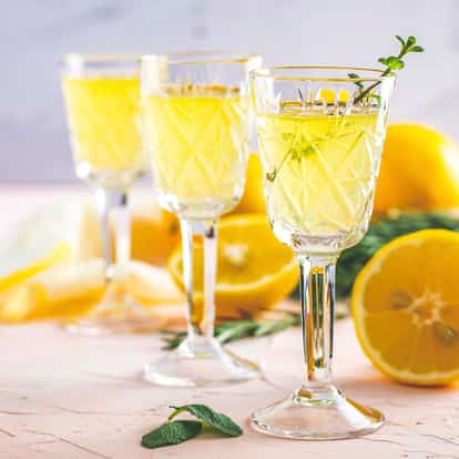 Strega in three etched cordial glasses with mint sprig and lemon halves on light background