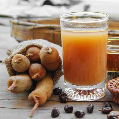 Tamarind Juice in a short glass with whole tamarind pods and a few seeds on a wooden table