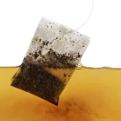 Used black tea bag partially submerged in brewed tea on white background
