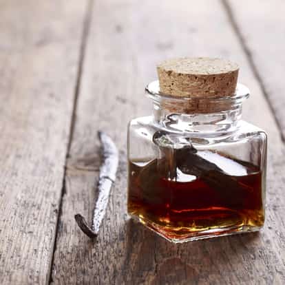Vanilla extract in a square glass jar with cork and a vanilla pod on a wooden board