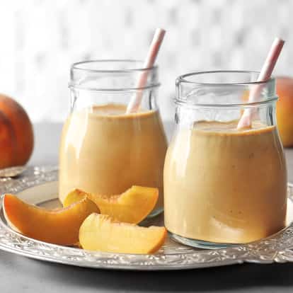 White Peach Puree in two glass jars with paper straws and peach wedges on a silver tray