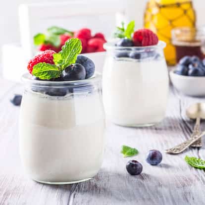 Yoghurt in two glass jars topped with blueberries raspberries and mint on a wooden surface