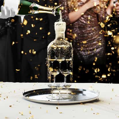 A champagne bottle being poured into glasses to create a champagne tower.