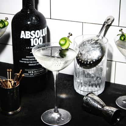 100 Cucumber Infused Martini served in chilled martini glass garnished with cucumber ribbon beside an Absolut 100 bottle