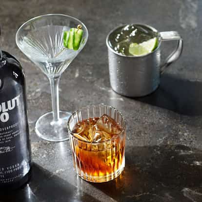100 Old Fashioned in a cut-glass rocks glass with ice and an Absolut 100 bottle beside it on stone surface