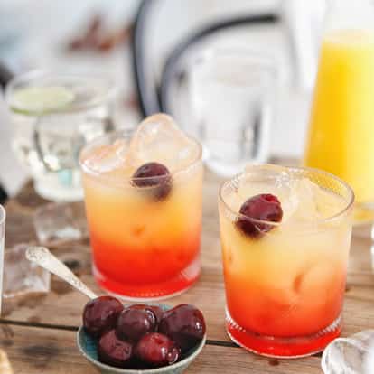 Absolut Apeach Surrender in two rocks glasses with ice and a cherry garnish on a wooden table