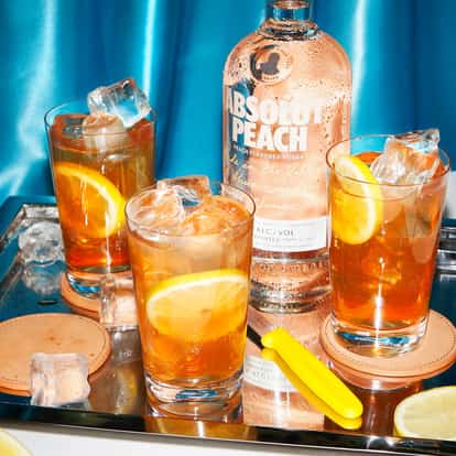 Absolut Apeach with Iced Tea three glasses with ice and lemon slices beside a peach vodka bottle on a tray