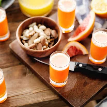 Absolut Bonobo served in multiple shot glasses on a wooden board with citrus wedges a bowl of nuts and a bottle at left