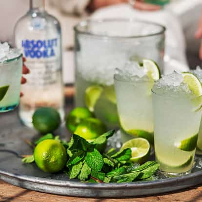 Absolut Caipiroska in highball glasses with crushed ice and lime wedges on a metal tray