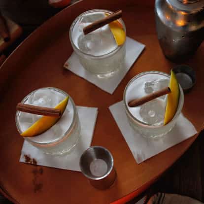 Absolut Cinnamango Sour served in rocks glasses on a tray garnished with mango slices and cinnamon sticks