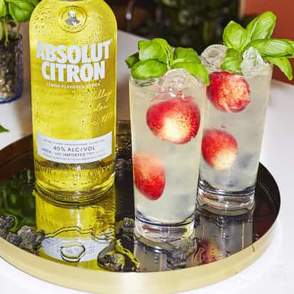 Absolut Citron Lemonade served in two tall glasses with ice and basil sprigs beside a bottle on a round tray