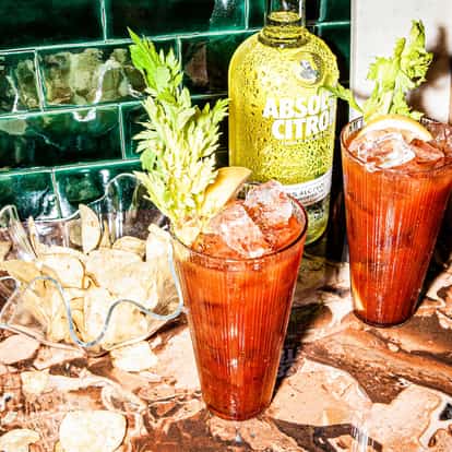Absolut Citron Bloody Mary in 2 tall ribbed glasses topped with ice lemon wedges and celery stalks on marble countertop