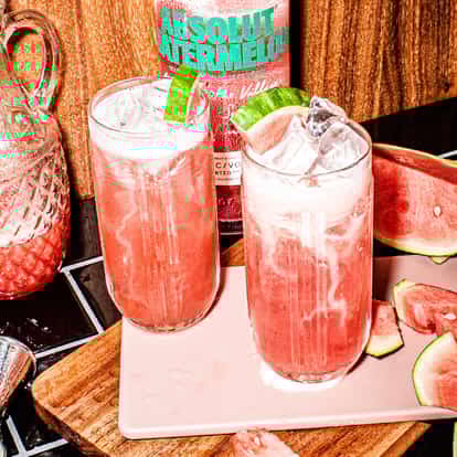 Absolut Fluffy Watermelon in two highball glasses with ice and watermelon wedges on a wooden board