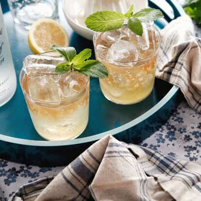 Absolut Fusion two short glasses with ice and a mint sprig on a tray beside a vodka bottle on cloth