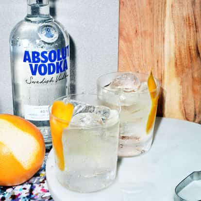 Absolut Gangster in a rocks glass with ice and grapefruit peel beside an Absolut Vodka bottle on a marble board