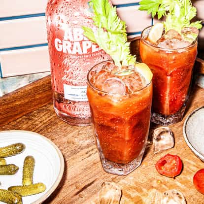 Absolut Grapefruit Bloody Mary in a highball glass with ice and celery stalk and lemon wedge on a wooden tray