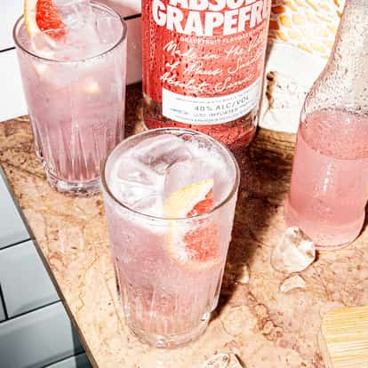 Absolut Grapefruit Fizzy in a highball glass with ice and a grapefruit wedge on a marble countertop