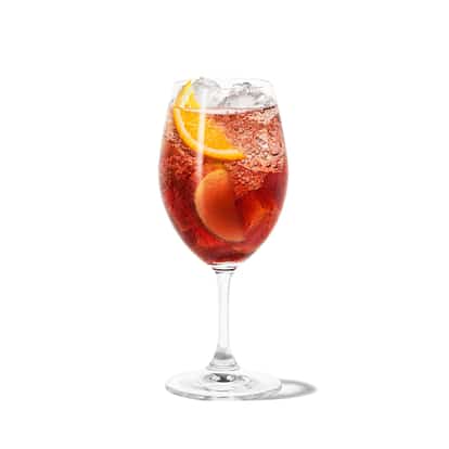Absolut Juice Apple Sangria in a stemmed wine glass with ice and orange and apple slices on white background