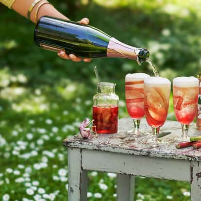 Absolut Juice Rhubarb Spritz served in three stemmed glasses with rhubarb ribbons and a bottle on a chipped table
